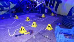 Crime scene investigation is set up, numbered cones and a plastic gun are scattered across the floor