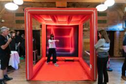 A lady is in a qube playing drop, a blindfolded challenge where the goal is to drop a red ball into a cylinder in ten seconds