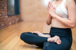 A close up of a woman doing yoga in lotus position as part of Yoga Team Building