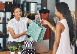 A woman sales assistant handing a woman a bag with items of clothing in.